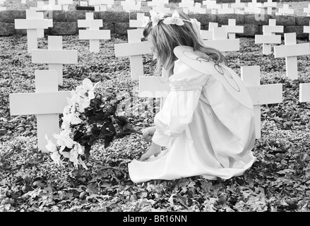 Une jeune fille comme un ange à genoux, placer des fleurs sur une tombe. Banque D'Images