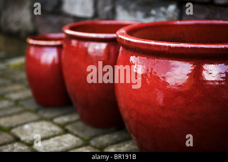 Close up Vue de côté trois pots de fleurs rouge vide sur les pavés en face de cité médiévale à mur de pierre. Banque D'Images