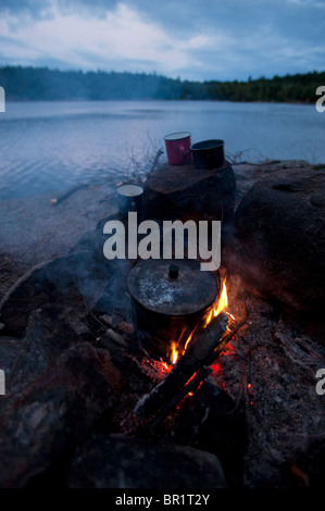 Enamel cups set sur les rochers autour d'un feu de camp, attendez que le pot à bouillir au Johnny Lake, le Parc provincial Killarney, Ontario Banque D'Images