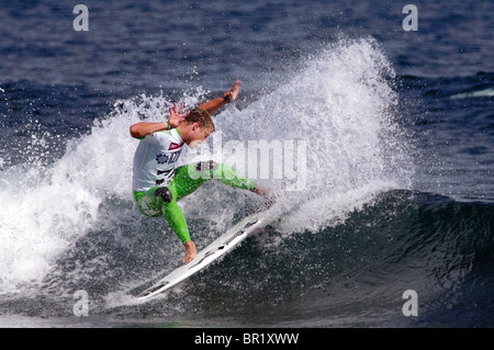 Un surfeur masculin en maillot jaune chevauche une vague lors d'une compétition de surf aux Açores, au Portugal. L'athlète s'équilibre dynamiquement sur la planche. Banque D'Images