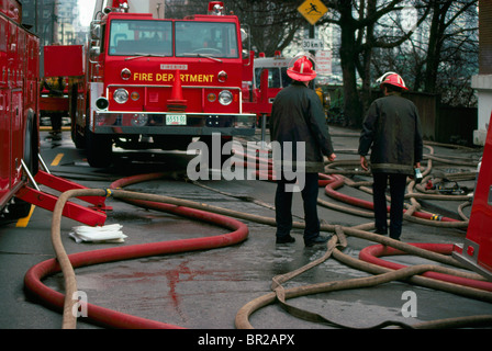 Pompiers Pompiers / comité permanent au milieu de tuyaux d'incendie et de camions, Vancouver, British Columbia, Canada Banque D'Images