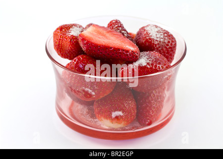 Close up de fraises dans un bol en verre, saupoudré de sucre et avec des fraises coupées en deux sur le dessus. fond blanc. Banque D'Images