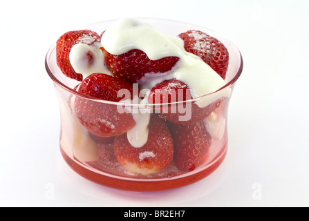 Close up de fraises dans un bol en verre, saupoudré de sucre et avec du yogourt sur le dessus. fond blanc. Banque D'Images