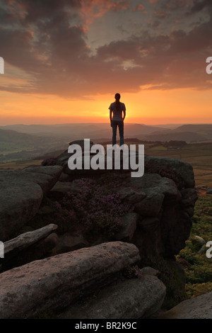 Silhouette d'une femme debout sur un éperon rocheux de Owler Tor près de Hathersage dans le Peak District de Derbyshire, Angleterre. Banque D'Images