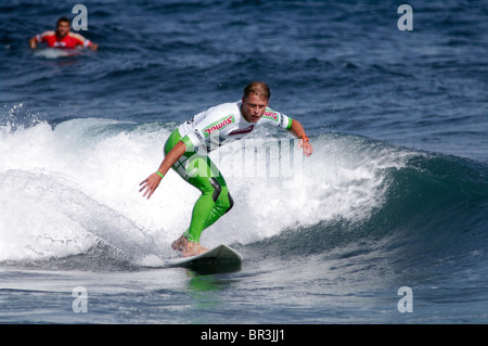 Un surfeur masculin en maillot jaune chevauche une vague lors d'une compétition de surf aux Açores, au Portugal. L'athlète s'équilibre dynamiquement sur la planche. Banque D'Images