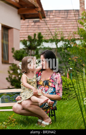 Mère fille avec l'implantation sur un banc dans le jardin - maison familiale en arrière-plan Banque D'Images