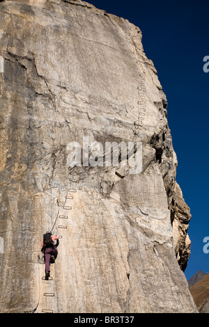 Une jeune femme monte une échelle intégrée à la falaise tout en s'engageant dans le sport de la Via Ferrata de Val d'isère, Savoie, France Banque D'Images