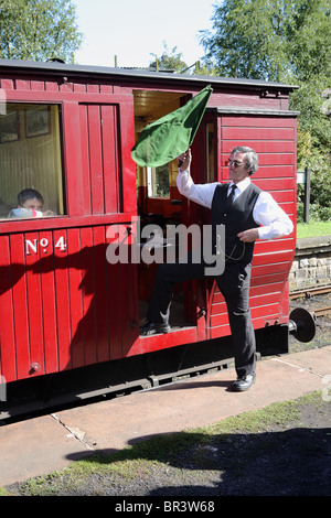 La garde d'un train à vapeur fer Tanfield signaux avec son drapeau vert qu'il est sûr de s'écarter de Andrews House Station, North East England, UK Banque D'Images