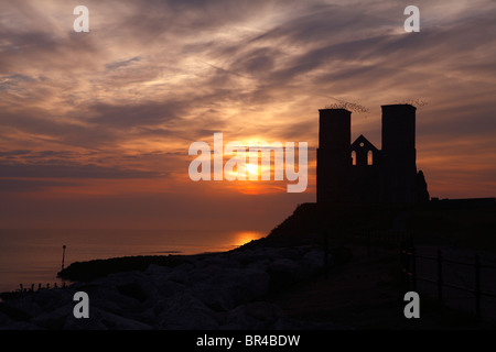 Lever du soleil à Reculver Tours et l''estuaire de la Tamise dans le Kent, un troupeau d'oiseaux décoller depuis le haut des tours. Banque D'Images