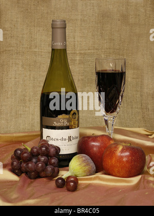 Bouteille de vin rouge et de vin dans un verre, avec des fruits sur un fond de toile. Banque D'Images