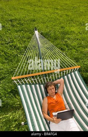 Senior woman with headset netbook et couché dans un hamac Banque D'Images