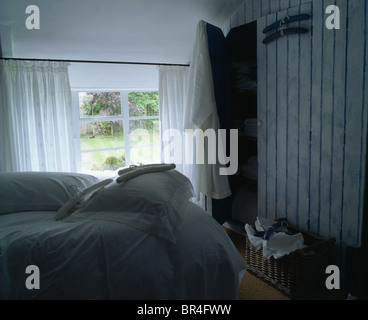 Rideaux voile blanc sur la fenêtre en chalet chambre avec armoire et lit avec draps et oreillers blanc Banque D'Images
