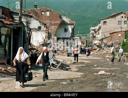 Les gens à pied la rue passé la destruction à Peja, au Kosovo. Banque D'Images