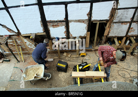 Rénovation d'un ancien bâtiment historique à pans de bois. Bricklayer formant un nouveau mur avec de vieilles briques et un charpentier formant de nouvelles poutres en chêne Banque D'Images