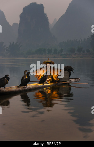 Le port de pêcheur La pêche avec manteau de paille sur les cormorans en radeau de bambou sur la rivière Li au crépuscule, Yangshuo, Guangxi, Chine Banque D'Images