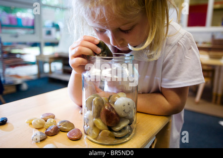 Une fille dans une école maternelle au Royaume-Uni la collecte de cailloux dans un pot de verre. Banque D'Images