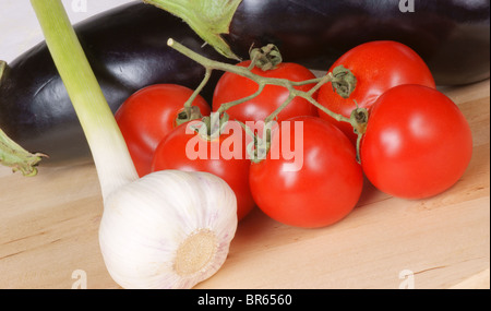 Les légumes biologiques frais, sur une planche à découper en bois : aubergines, l'ail et les tomates. Studio shot Banque D'Images