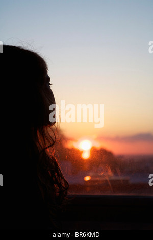Une jeune fille regarder par la fenêtre au coucher du soleil Banque D'Images