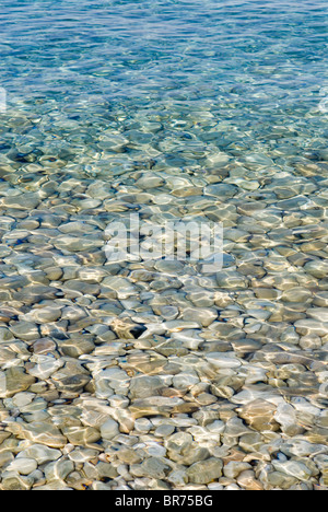 Le soleil brille à travers la mer, sur de petits cailloux sur une plage de Paxos, Grèce Banque D'Images