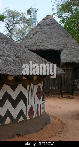 La boue et traditionnelles au toit de maison s'asseoir en face d'une tour de communications de la ville de Victoria Falls au Zimbabwe. Banque D'Images