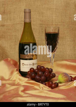 Bouteille de vin rouge et de vin dans un verre, avec des fruits sur un fond de toile. Banque D'Images