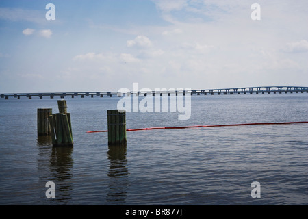 Boom de l'huile rouge dans l'eau dans une baie tranquille avec des pieux en bois et un littoral rocheux le long de la Côte du Golfe. Banque D'Images