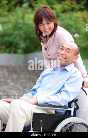 Young couple in park, woman pushing man in wheelchair Banque D'Images