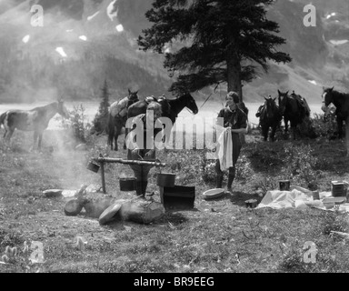 Années 1920 Années 1930 DEUX FEMMES À LA PRÉPARATION DES ALIMENTS CUISINE FEMME CAMPING CAMP Plus de chevaux avec équipement d'équitation en arrière-plan Banque D'Images