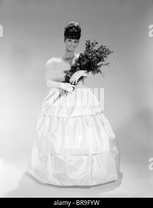 1960 jolie jeune femme en robe de soirée CONCOURS DE BEAUTÉ À PORTER DE LA FOURRURE A VOLÉ ET TIARA HOLDING BOUQUET DE ROSES À LA RECHERCHE À Banque D'Images