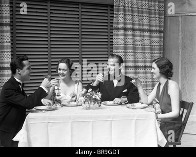 1930 DÎNER deux couples en robe de soirée formelle TOASTING Banque D'Images