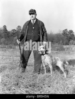 1930 MAN STANDING IN FIELD HOLDING SHOTGUN ET UNE LAISSE DE CHIEN SETTER GORDON Banque D'Images