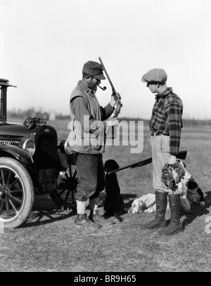 Années 30, DEUX HOMMES EN VOITURE À LA RECHERCHE DE CHASSEURS AVEC DES CHIENS DE CHASSE ET LE RENFORT D'OISEAUX Banque D'Images