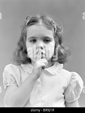Années 1940 Années 1950 GIRL AVEC LES DOIGTS POUR FAIRE DE GESTE CHUT CALME LÈVRES LOOKING AT CAMERA Banque D'Images