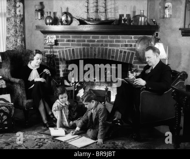 1930 FAMILLE DE QUATRE ASSIS DEVANT CHEMINÉE Mère Père PIPE LECTURE TRICOT ENFANTS À FAIRE LEURS DEVOIRS Banque D'Images