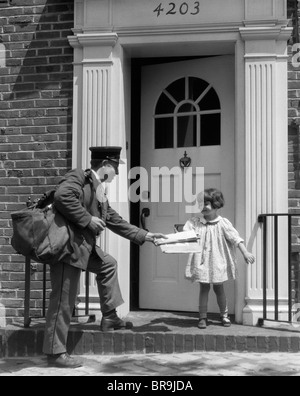 Années 1920 SMILING LITTLE GIRL DE RECEVOIR DU COURRIER DE POSTMAN Banque D'Images