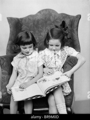 Années 1920 Années 1930 deux filles assises côte à côte dans PRÉSIDENT READING BOOK Banque D'Images