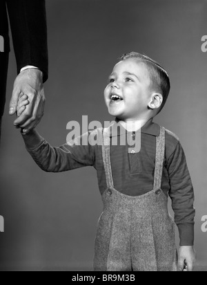 1960 BOY HOLDING HOMME ADULTE PART SMILING Banque D'Images