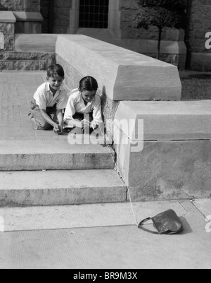 1930 DEUX JEUNES GARÇONS JOUENT AU TOUR AVEC STRING LIÉE À PERDU SAC À MAIN Banque D'Images