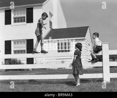 1950 garçon marcher en équilibre sur une clôture d'autres enfants assis à côté de l'article clôture Banque D'Images