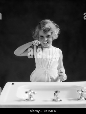 1930 enfant cheveux bouclés BLOND GIRL SE BROSSER LES DENTS, BROSSE À DENTS, LOOKING AT CAMERA Banque D'Images