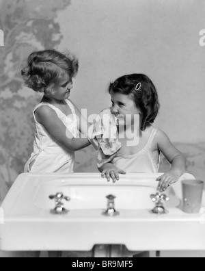 Années 1930 DEUX FILLES SOEURS au lavabo de la salle de bains Banque D'Images