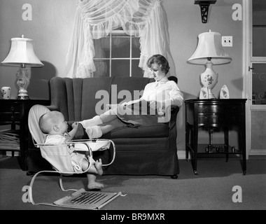 1950 Baby Sitter Adolescents Assis Sur Le Canape Tandis Que Dans La Lecture De Manuels Scolaires Bebe Elingue S Empare De Son Fauteuil Gonflable Cale Pied Photo Stock Alamy