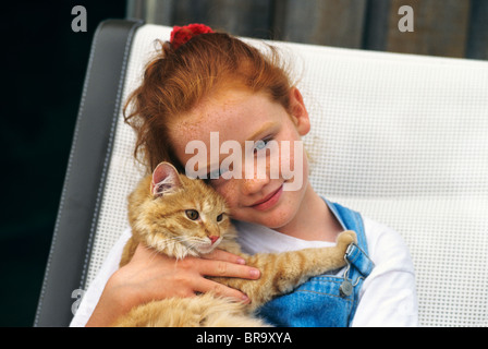 LITTLE RED HEAD GIRL HOLDING ORANGE TABBY CAT Banque D'Images