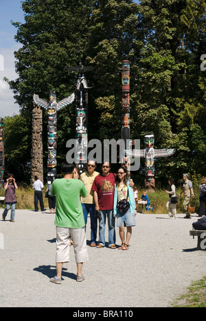 Les touristes posent pour une photo devant des poteaux totémiques sculptés dans le Stanley Park à Vancouver, en Colombie-Britannique. Banque D'Images