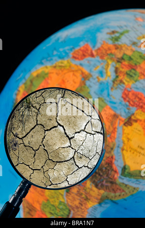 La terre craquelée par la sécheresse vu à travers une loupe tenu contre allumé globe terrestre Banque D'Images