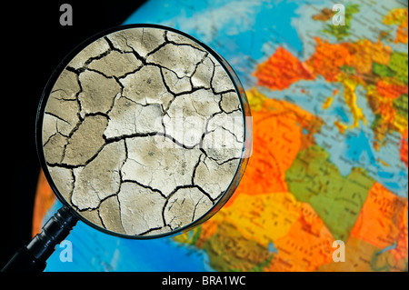 La terre craquelée par la sécheresse vu à travers une loupe tenu contre allumé globe terrestre Banque D'Images