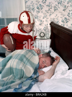 1960 garçon en uniforme de football se réveiller PÈRE ENDORMI DANS LA CHAMBRE PISCINE NOSTALGIE MAN Banque D'Images