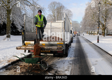 Un ouvrier de pelles de sable de l'arrière d'un camion dans une brouette sur une route couverte de neige dans la région de Tettenhall, Wolverhampton. Banque D'Images