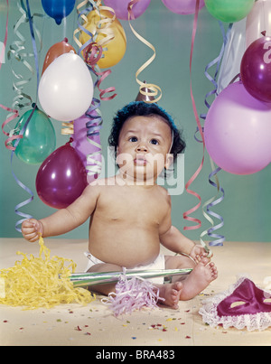 1960 AFRICAN-AMERICAN BABY BOY WEARING PARTY HAT BALLOONS BANDEROLLES CRÉCELLE MASK Banque D'Images