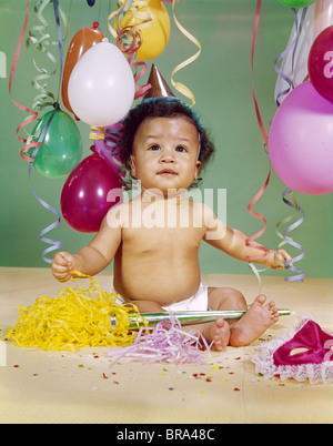 1960 AFRICAN-AMERICAN BABY BOY WEARING PARTY HAT BALLOONS BANDEROLLES CRÉCELLE MASK Banque D'Images